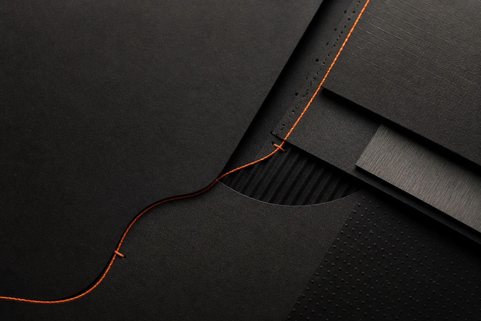 Layered black technical materials joined by an orange thread